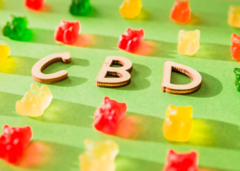 Wooden letters CBD on a green background and gelatin in the form of bears.