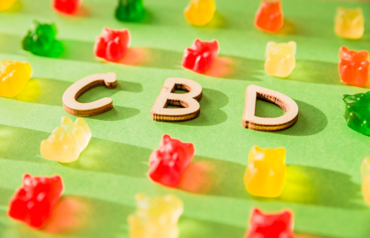 Wooden letters CBD on a green background and gelatin in the form of bears.